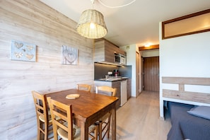 Una mesa de madera con sillas, una zona de cocina con microondas y una cama con cabecero de madera.