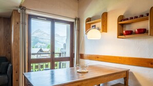 Een houten tafel met een lamp, een bank, een raam met uitzicht op bergen en houten planken met rode kommen.