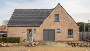 A single-story brick building with a dark grey roof, a central entrance door, and a garage door. - Villa Mira is a Very Pleasant and Modern Villa (Koksijde)