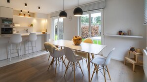 A modern kitchen with white cabinetry, a dining area with a white table and chairs, and a view of the outdoors through large windows. - Villa Mira is a Very Pleasant and Modern Villa (Koksijde)