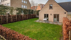 A residential property with a well-maintained lawn, a small patio area with a table and chairs, and a brick house with a sloped roof. - Villa Mira is a Very Pleasant and Modern Villa (Koksijde)