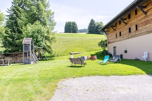 Un espace extérieur verdoyant avec un bâtiment en bois, une cabane de jeux en bois et des sièges pour se détendre à l’extérieur.