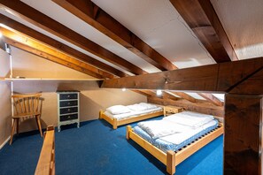 A small attic bedroom with two wooden beds, a chair, and a dresser.
