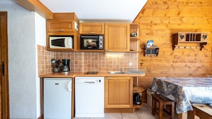 A compact kitchen with wooden cabinets, a microwave, a dishwasher, and a small table with a tablecloth. - Apartment 'Le Lachat' with Mountain View, Shared Terrace and Wi-Fi (Cohennoz)