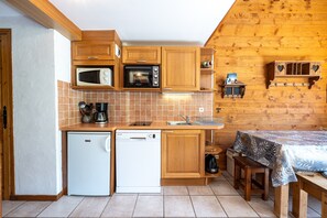 A compact kitchen with wooden cabinets, a microwave, a dishwasher, and a small table with a tablecloth. - Apartment 'Le Lachat' with Mountain View, Shared Terrace and Wi-Fi (Cohennoz)