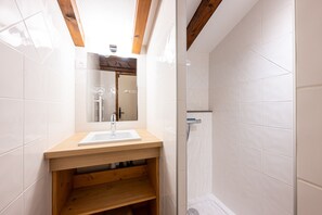 A bathroom with a wooden vanity, a mirror, a sink, and a shower area.