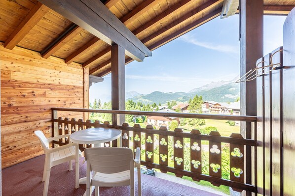 A wooden balcony with a table and chairs, overlooking a mountainous landscape.