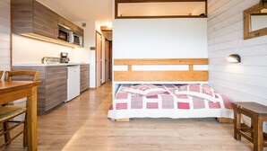 Une petite pièce comprenant un lit, une table en bois, un coin cuisine et un miroir au mur.