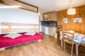 Ein kleines Zimmer mit Bett, Küchenzeile, Essbereich und Holzwänden.