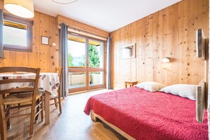 A wooden-paneled room with a bed, a table with a tablecloth, a chair, and a window with curtains.
