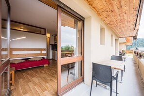 A room with a wooden ceiling, a sliding glass door, a sofa, a table with chairs, and a view of the outdoors.