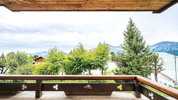 Een balkon met houten hekwerk, een betonnen rand en uitzicht op bergen en bomen.
