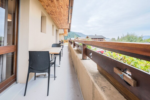 A balcony with a wooden railing, a table, and chairs.