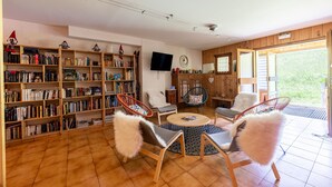 Een woonkamer met boekenplanken, een televisie en twee fauteuils met zachte kussens.