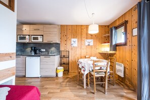 Eine kompakte Küche mit Holzausstattung, einer Mikrowelle, einer Kaffeemaschine und einem Essbereich mit Tisch und Stühlen.