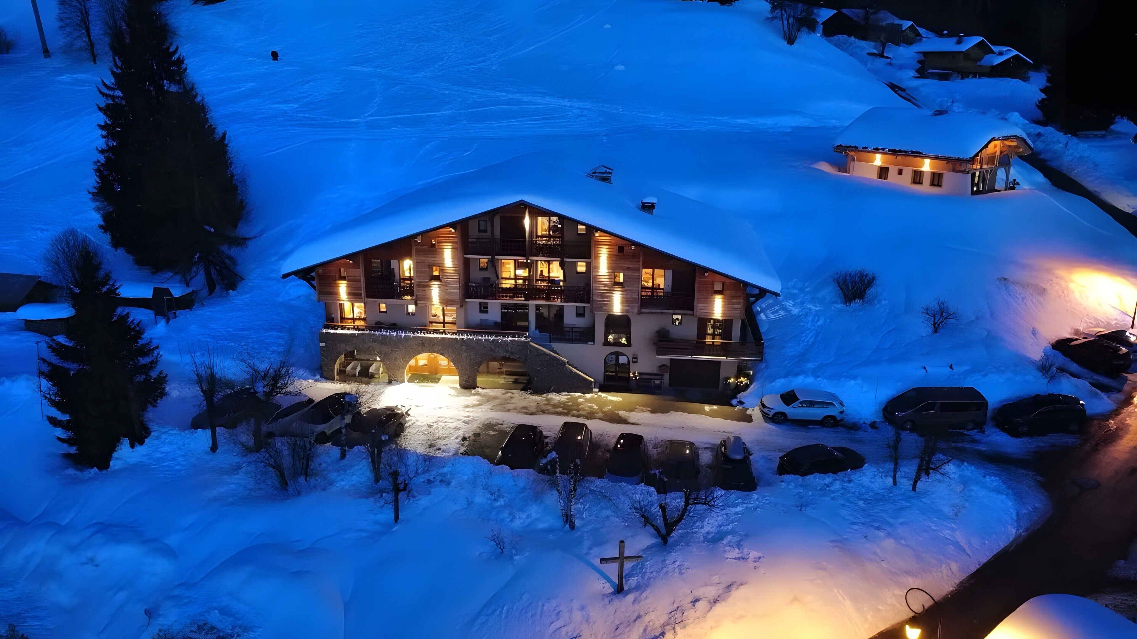 A snow-covered lodge with a large central building, a stone bridge, and parked cars.