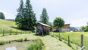 Eine ländliche Landschaft mit einem Holzstall, einem eingezäunten Feld und einem kleinen Teich.
