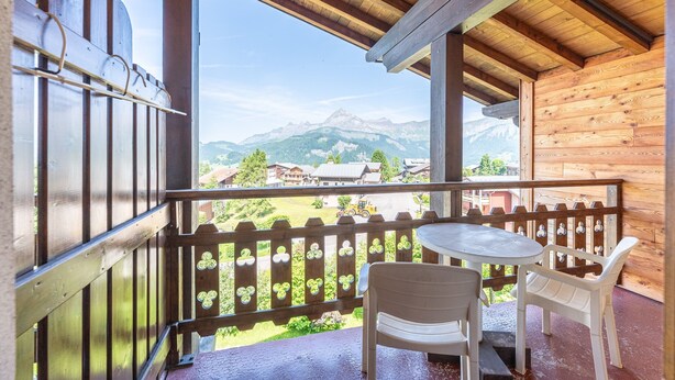 Ein Holzbalkon mit Tisch und Stühlen, mit Blick auf eine Berglandschaft.