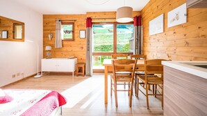 A wooden interior with a dining area, a sink, and a window with a view of a green landscape. - Studio Apartment '2 - L'Edelweiss' with Mountain View, Shared Garden and Wi-Fi (Cohennoz)