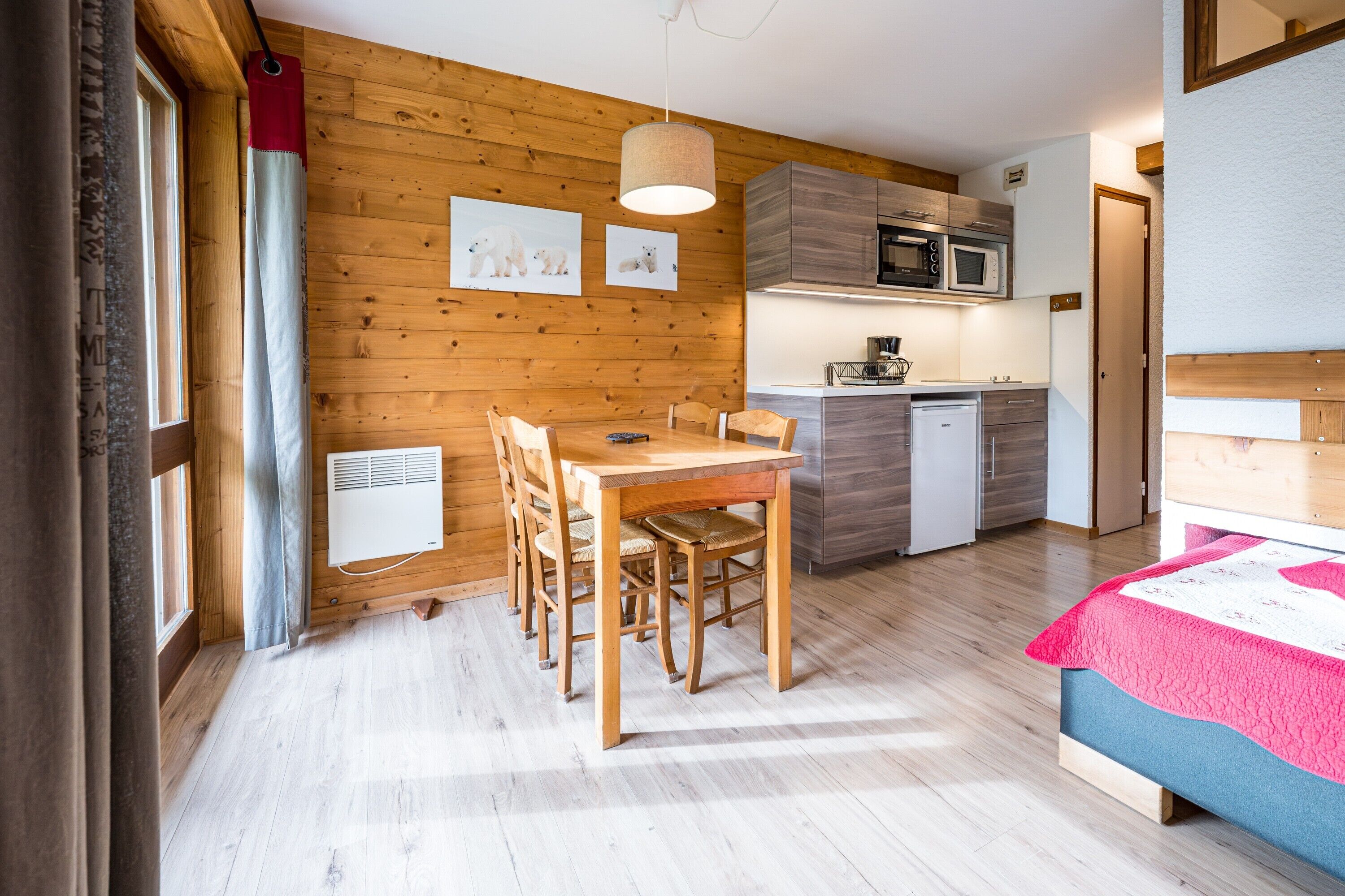 Una stanza compatta con un tavolo da pranzo in legno, sedie, un letto, angolo cottura e una finestra con tende.