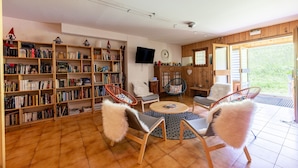 A living room with bookshelves, a television, and two chairs with fluffy cushions. - Studio Apartment '2 - L'Edelweiss' with Mountain View, Shared Garden and Wi-Fi (Cohennoz)