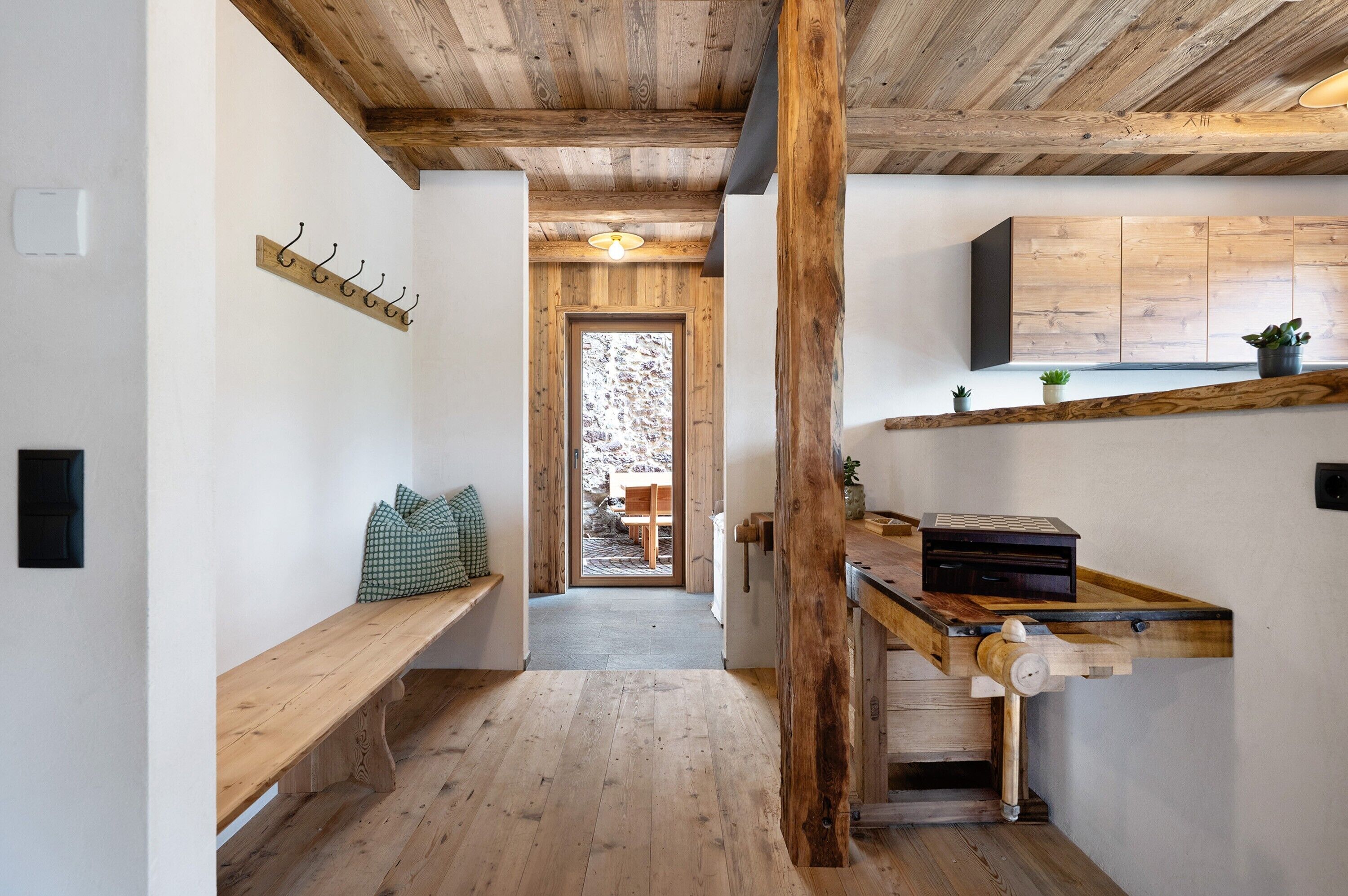 Ambiente in legno con una panca, un armadietto e una porta che dà su uno spazio esterno.