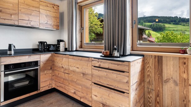 Uma cozinha com armários de madeira, forno embutido e janela com vista para uma paisagem verde.