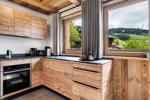 A kitchen with wooden cabinets, a built-in oven, and a window with a view of a green landscape. - Chalet 'Wellness  Samer' with Mountain View, Private Terrace and Wi-Fi (Sarentino)