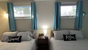 A room with two beds, each with a pillow featuring a word. There is a nightstand with a lamp and a small plant. - Studio #2 On Lake Superior, Water Views and Outdoor Adventure Await! (Paradise)