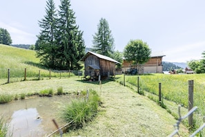 Paisaje rural con un granero de madera, un campo cercado y un pequeño estanque.