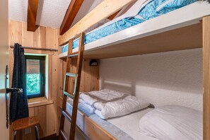 Une chambre avec un lit superposé, une échelle, une fenêtre avec des rideaux et un petit tabouret en bois.