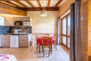 Una cocina compacta con electrodomésticos modernos, una zona de comedor con mantel rojo y paredes de madera.