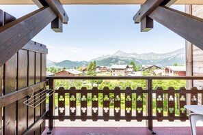 A balcony with a wooden railing, a white chair, and a view of houses and mountains in the background. - Studio Apartment '13 - L'Étale' with Mountain View, Shared Garden and Wi-Fi (Cohennoz)