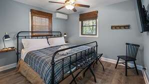 Ein Schlafzimmer mit Bett, Deckenventilator, Fernseher, Stuhl und einem Fenster mit Jalousien.