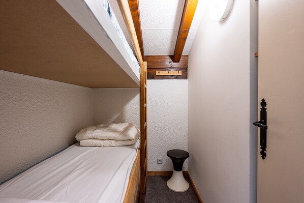 A small, narrow room with a bunk bed, a small round table, and a door with a black handle.