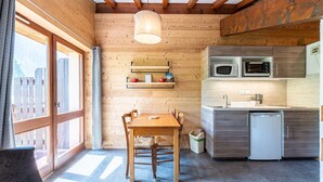 A wooden interior with a dining table, chairs, a kitchen with a microwave, and a small refrigerator.