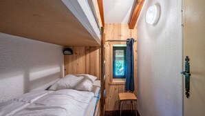 Een kleine slaapkamer met een eenpersoonsbed, een raam met gordijnen en een deur met een decoratieve handgreep.