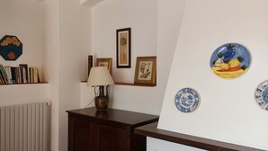 Una stanza con termosifone, libreria, lampada e decorazioni murali tra cui quadri incorniciati e piatti in ceramica.