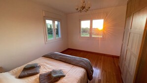 Un dormitorio con dos ventanas, una cama con manta y almohadas, y un candelabro.