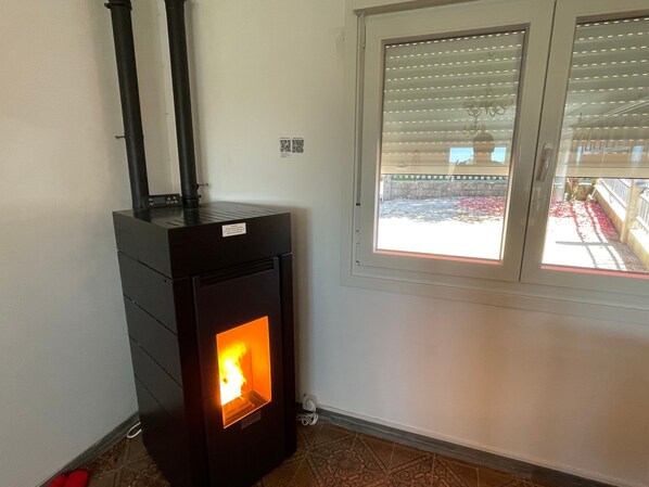 A room with a wood-burning stove, a window with blinds, and a tiled floor.