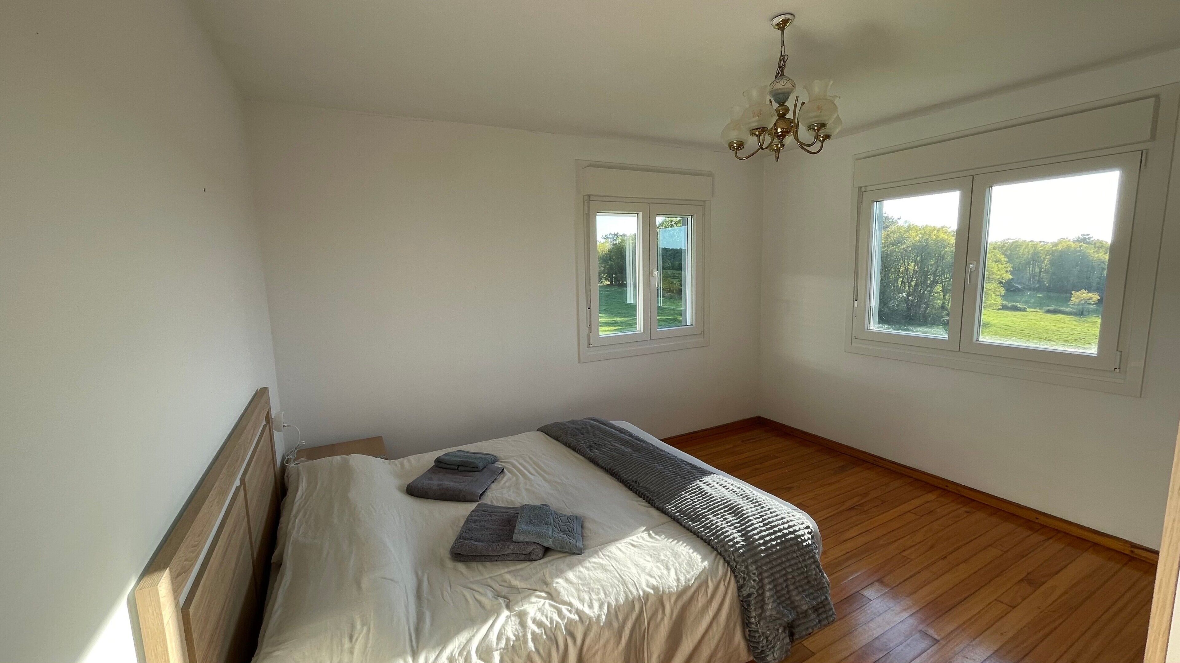 A bedroom with a bed, two windows, and a chandelier.