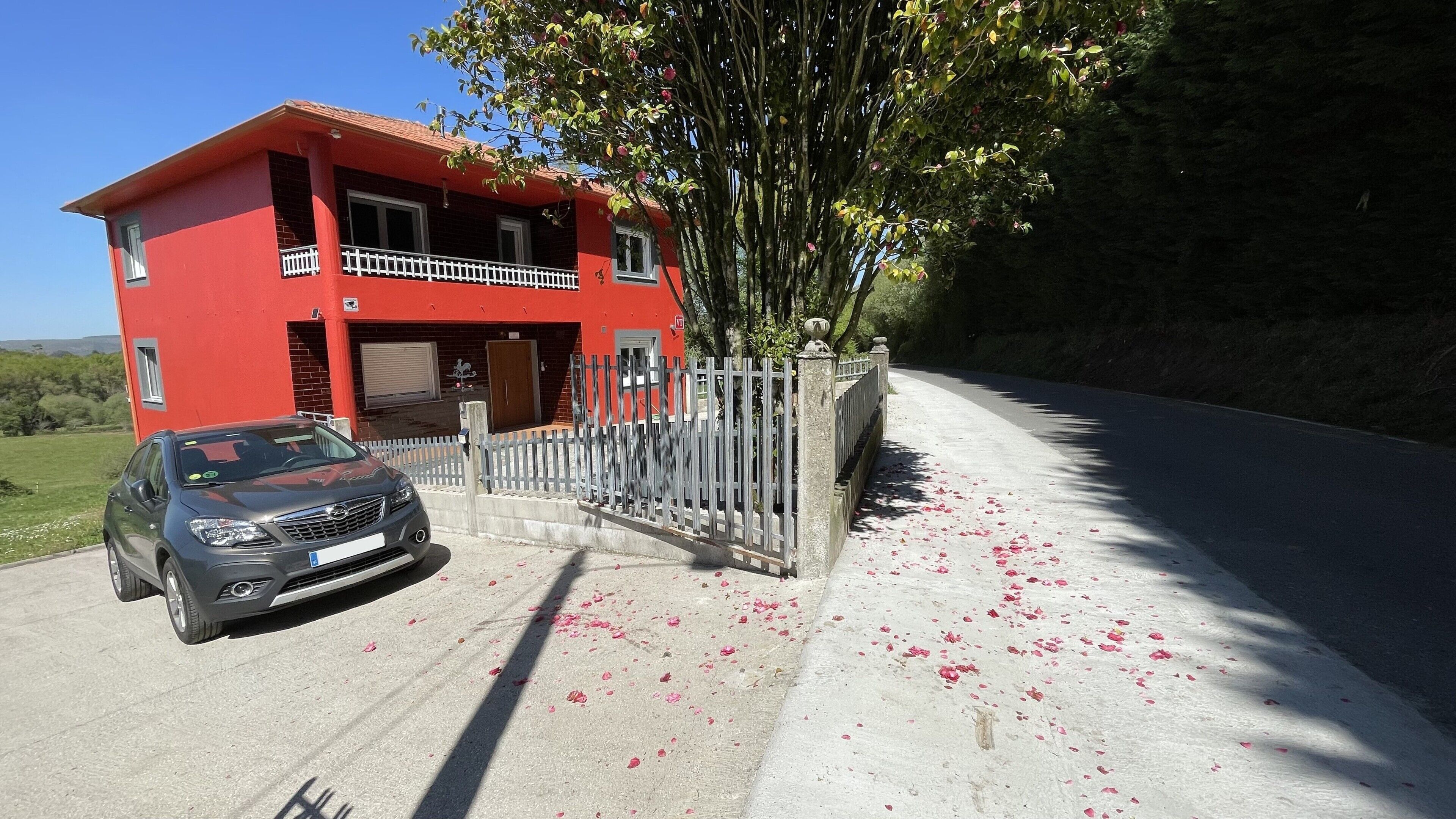 A red building with a balcony, a car parked in front, and scattered rose petals on the ground.