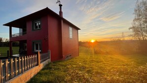 Una casa roja de dos pisos con una chimenea visible, un balcón y un patio cercado.