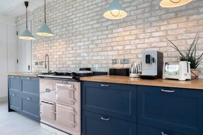 A kitchen with a brick wall, a stove, a toaster, and pendant lights. - The Old Dairy: A Stunning Detached Rural Retreat (Crudwell)
