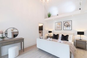 A modern bedroom with a bed, bedside tables, a desk, and a mirror.