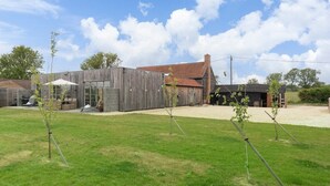 A rustic building with a wooden exterior, a covered outdoor seating area, and a fenced yard with young trees.