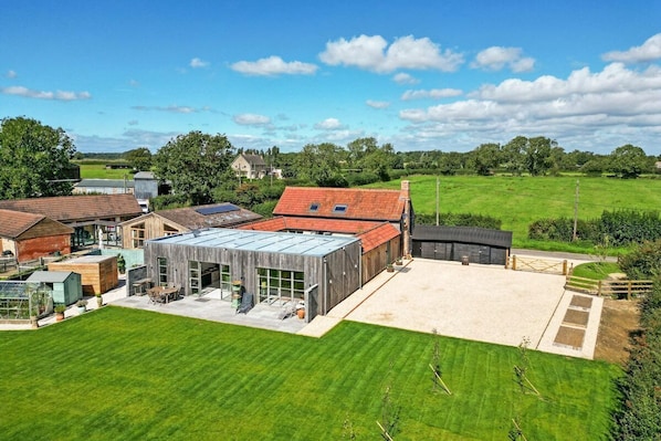 A modern house with a large glass conservatory, a spacious patio, and a well-maintained lawn.