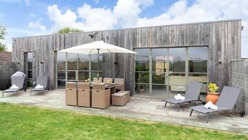 Un patio al aire libre con sillones, una mesa y una zona de parrilla.