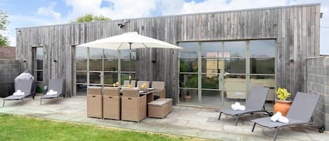En udendørs terrasse med loungesæder, et bord og grillområde.