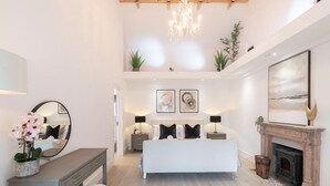 A modern bedroom with a large bed, bedside tables, a mirror, a fireplace, and artwork on the walls.
